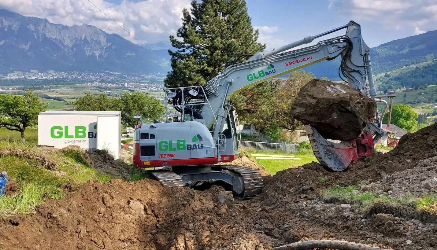 A GLB Bau excavator working on a hillside building site, with mountains behind it